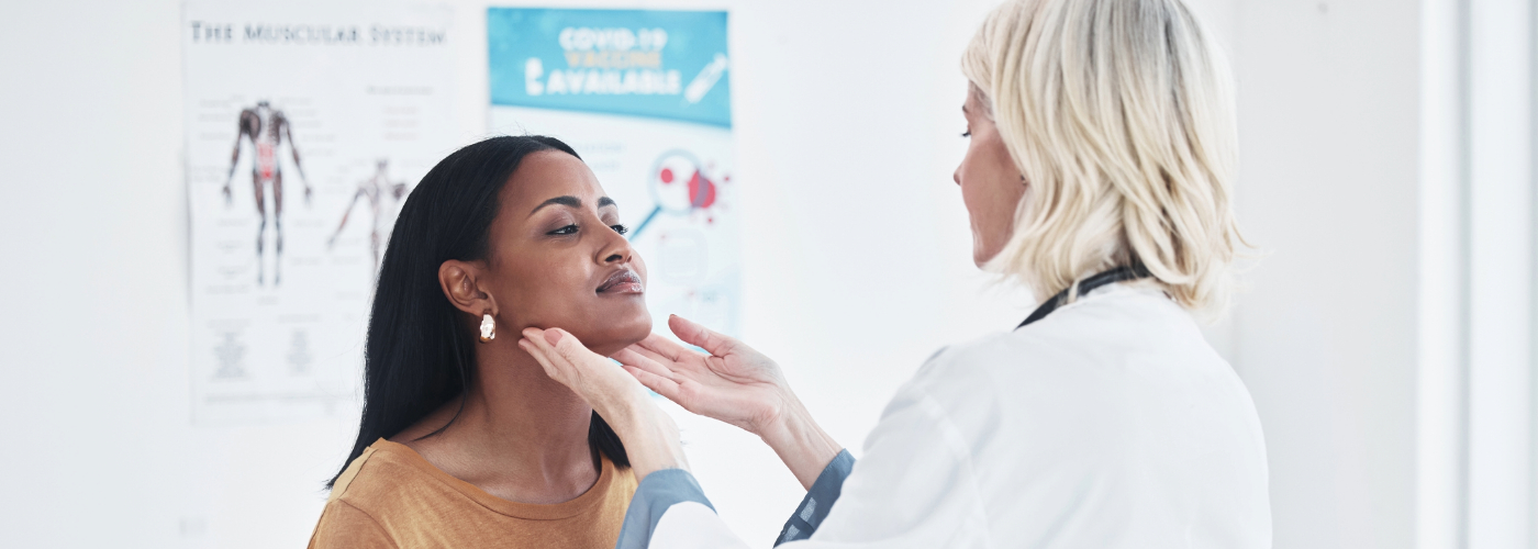 Doctor examining a woman's thyroid in a doctors office.